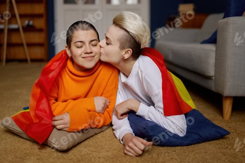 Preview: Loving lesbian couple posing together with rainbow multicolored flag