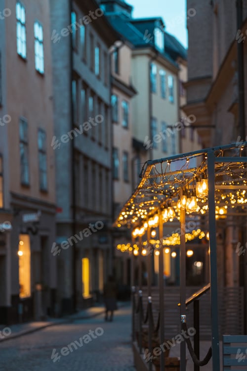 Preview: Light bulbs of a street cafe in the evening with old town buildings in the background.