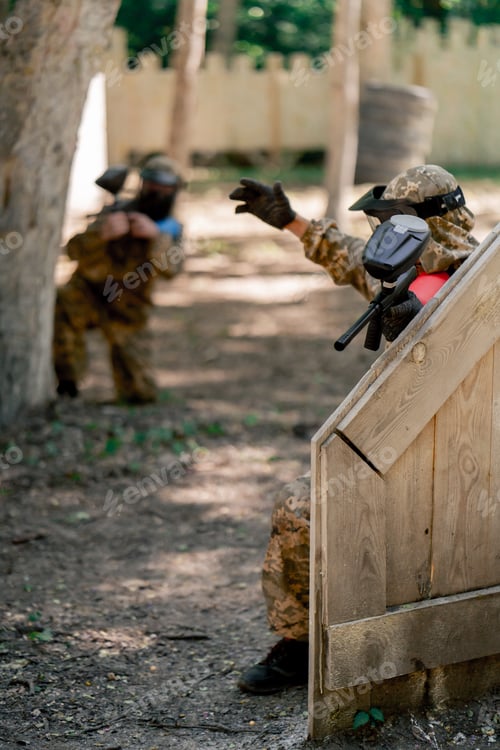 Preview: in the wild near tree structures player in a pintball uniform holds a pistol with a balloon team