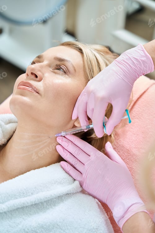 Preview: Partial female cosmetologist doing neck beauty injection with syringe of woman