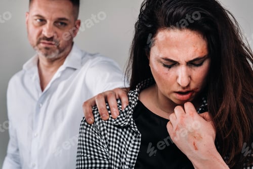 Preview: A woman beaten by her husband standing behind her and looking at her aggressively. Domestic violence