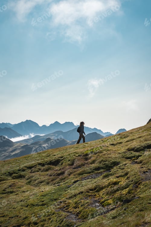 Preview: A person is leisurely strolling up a grassy slope in the scenic mountains