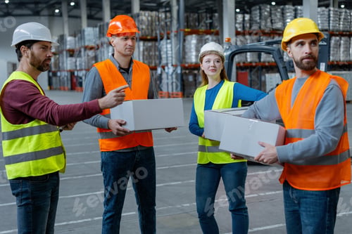 Preview: Group of successful workers wearing safety helmets and workwear holding boxes, looking away