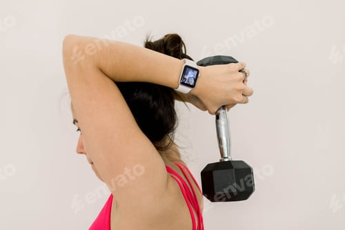 Preview: Young woman wearing an Apple Watch and lifting weights at a home gym