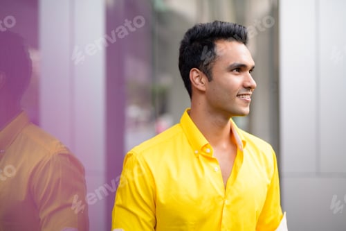 Preview: Profile view of happy young handsome Indian man smiling in the city
