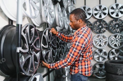 Preview: African american Car mechanic holding car rims ready to mount the wheels in workshop