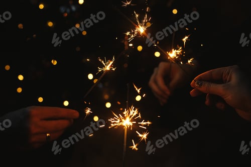 Preview: Hands holding fireworks against christmas lights in dark room. Happy New Year! Atmospheric holiday