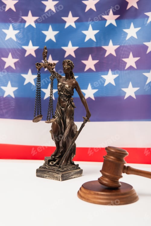 Preview: wooden gavel and statuette of justice near american flag on background