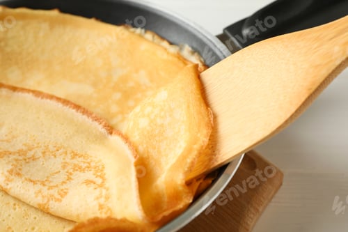 Preview: Pan with tasty thin pancakes and spatula on wooden table