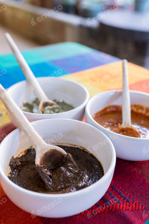 Preview: Three bowls with red, green and yellow mole sauce on top of a colorful traditional tablecloth