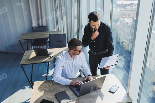 Preview: Two business men are creating a project while looking at the laptop screen during a meeting