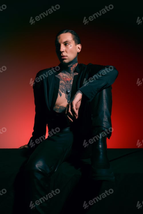 Preview: Stylish young man with tattoos posing in dramatic lighting against a vibrant red backdrop
