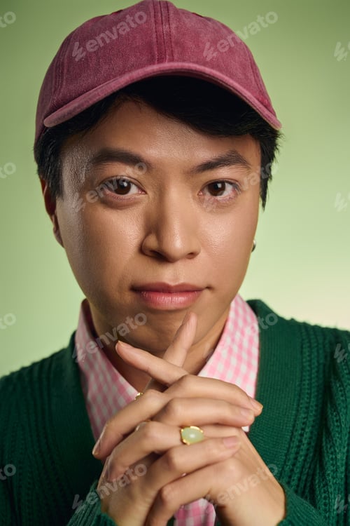 Preview: Stylish asian man showcases modern fashion in a vibrant green studio setting