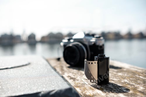 Preview: A 35mm roll film is on a banister with an out of focus analog camera behind.