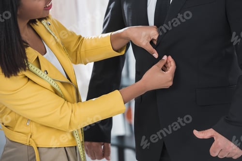 Preview: cropped shot of smiling tailor fitting man in formal wear indoors