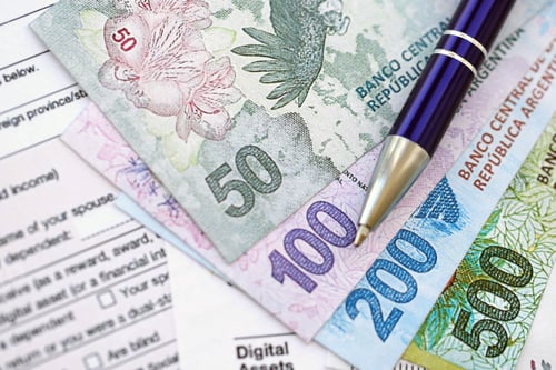 Preview: Argentine pesos money bills in big amount lies on table with pen and tax forms close up