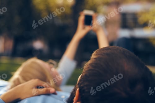Preview: A man and a woman lie in the park on the grass with a phone in their hands rest communication