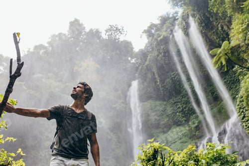 Preview: Young man standing near a waterfall in forest