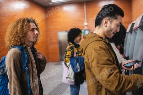 Preview: Young tourists using mobile phone to buy train tickets at station