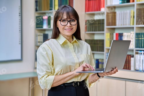 Preview: Middle aged elegant woman using laptop inside library
