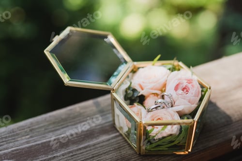 Preview: Closeup of two wedding rings and an engagement ring in a vintage box with flower petals.