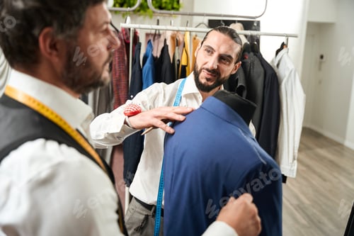 Preview: Tailor Adjusting Blue Jacket on Mannequin in Studio