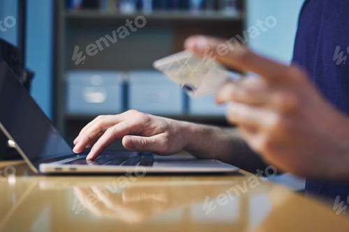 Preview: Close-up hands of person during online shooping. Young man holding credit card and using laptop.
