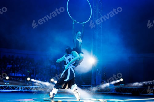 Preview: Aerialist performs on a gymnastic hoop under dome of the circus under the light of blue spotlights.
