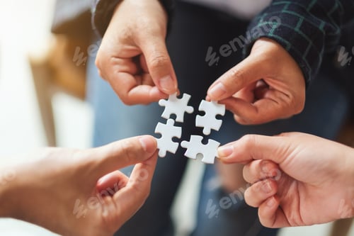 Preview: Closeup image of a group of people holding and putting a piece of white jigsaw puzzle together