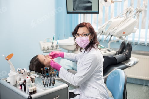 Preview: Female dentist with dental tools - mirror and probe treating patient teeth at dental clinic office
