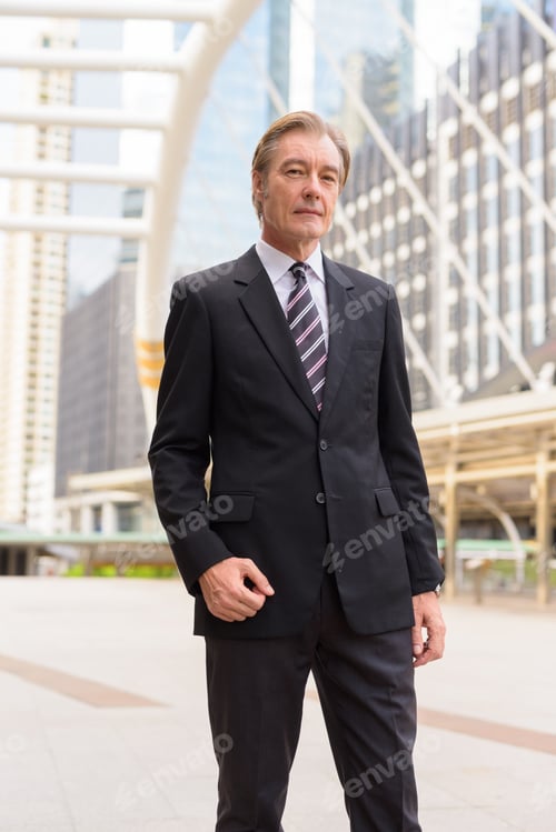 Preview: Mature handsome businessman in suit at skywalk bridge in the city