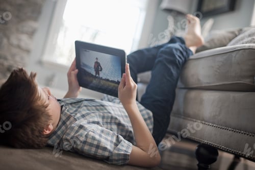 Preview: A boy lying on his front on the floor, looking at a digital tablet.