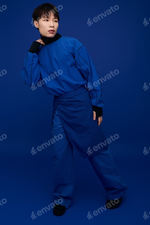 Preview: Young handsome Asian man poses stylishly against a deep blue backdrop showcasing modern fashion