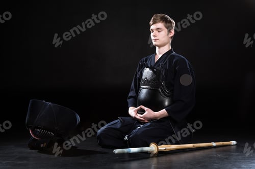 Preview: Young man in kendo armor sitting with closed eyes on black