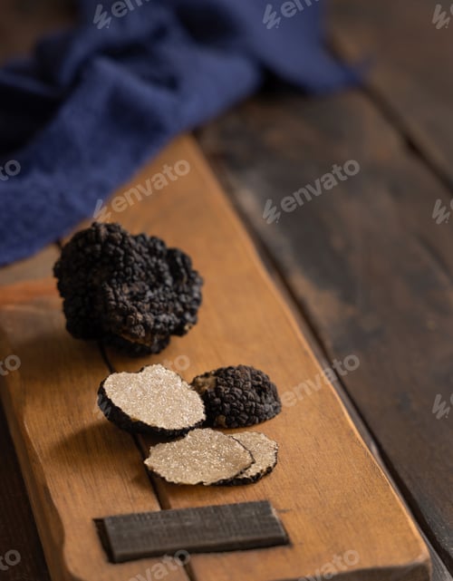 Preview: Whole and sliced black truffles mushroom on wooden board on dark brown table, close up