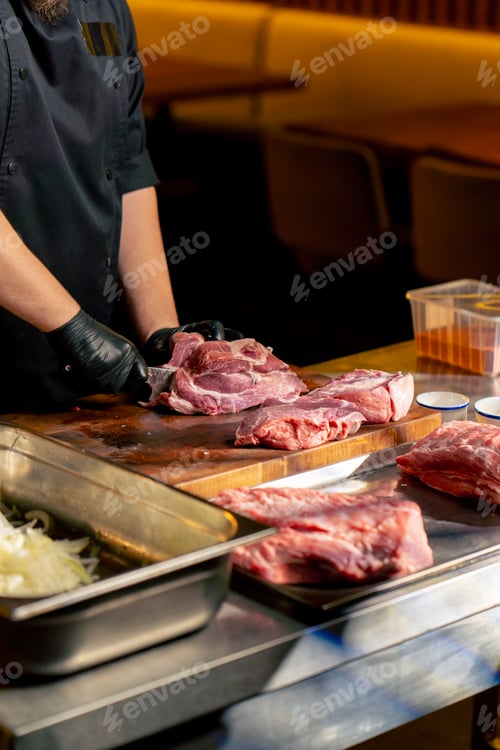 Preview: in a restaurant in a rib bar in the central hall, a chef in black gloves cuts large piece of pork