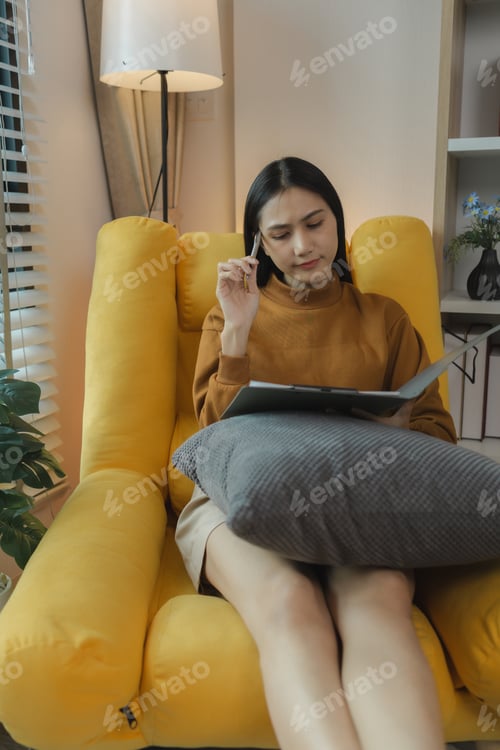 Preview: An Asian woman is sitting on the sofa in the living room, checking work she brought home for the wee