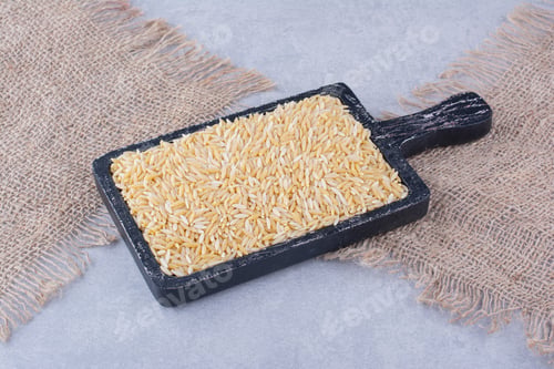 Preview: Worn-out black tray stocked with brown rice on marble background