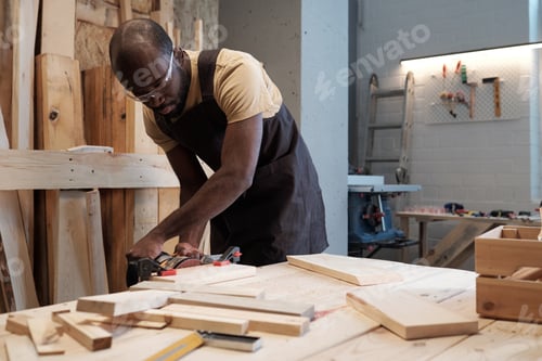 Preview: Portrait of mature black man building wooden furniture in carpentry workshop, copy space