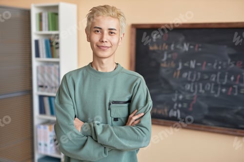 Preview: Young smiling Asian man in grey pullover crossing his arms by chest