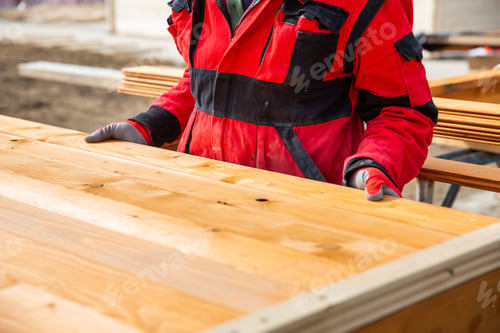 Preview: Construction worker in red workwear working with a wooden structure on a construction site.