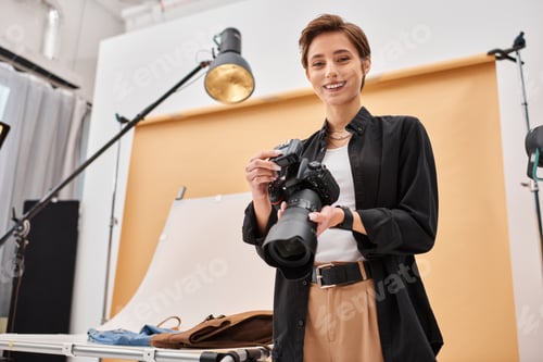 Preview: cheerful attractive woman with photography equipment smiling happily at camera in her studio