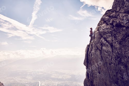 Preview: Hiker standing on a cliff edge overlooking scenic mountain views under a vast sky