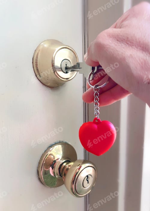 Preview: Woman homeowner unlocking & opening golden door knob at her home door with a key in a heart keychain