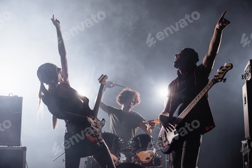 Preview: KYIV, UKRAINE - AUGUST 25, 2020: Rock band guitarists with hands in air singing with smoke and