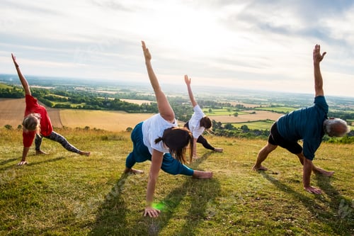 Preview: Group of women and men taking part in a yoga class on a hillside.