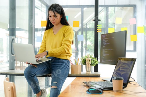 Preview: Asian female programmer sit on shelves and look at the laptop screen on their leg.