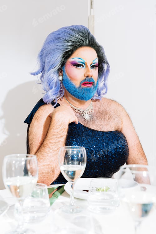 Preview: Drag Queen with blue beard sitting at served table