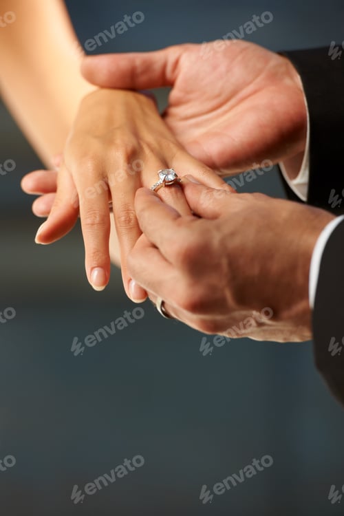 Preview: Making a vow. Cropped view of a groom slipping a ring on to his brides finger.