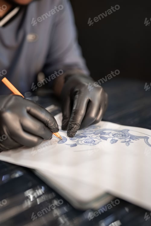 Preview: A tattoo artist is drawing a design stencil on his work stretcher before tattooing